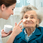 A woman is putting cream on the face of an older person.